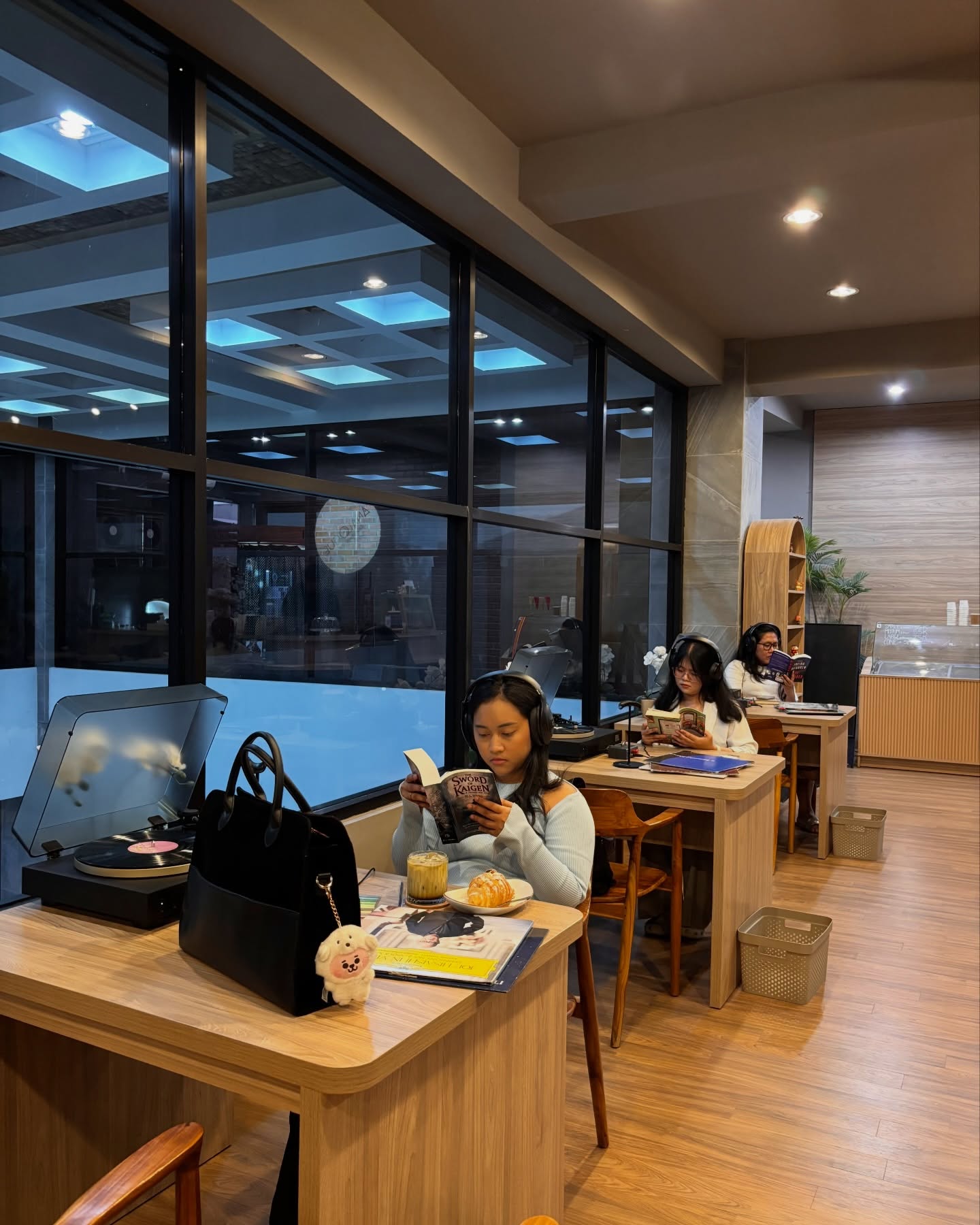 Tiga peserta berheadphone membaca sendiri-sendiri di meja berderet tepi jendela, masing-masing dengan turntable.