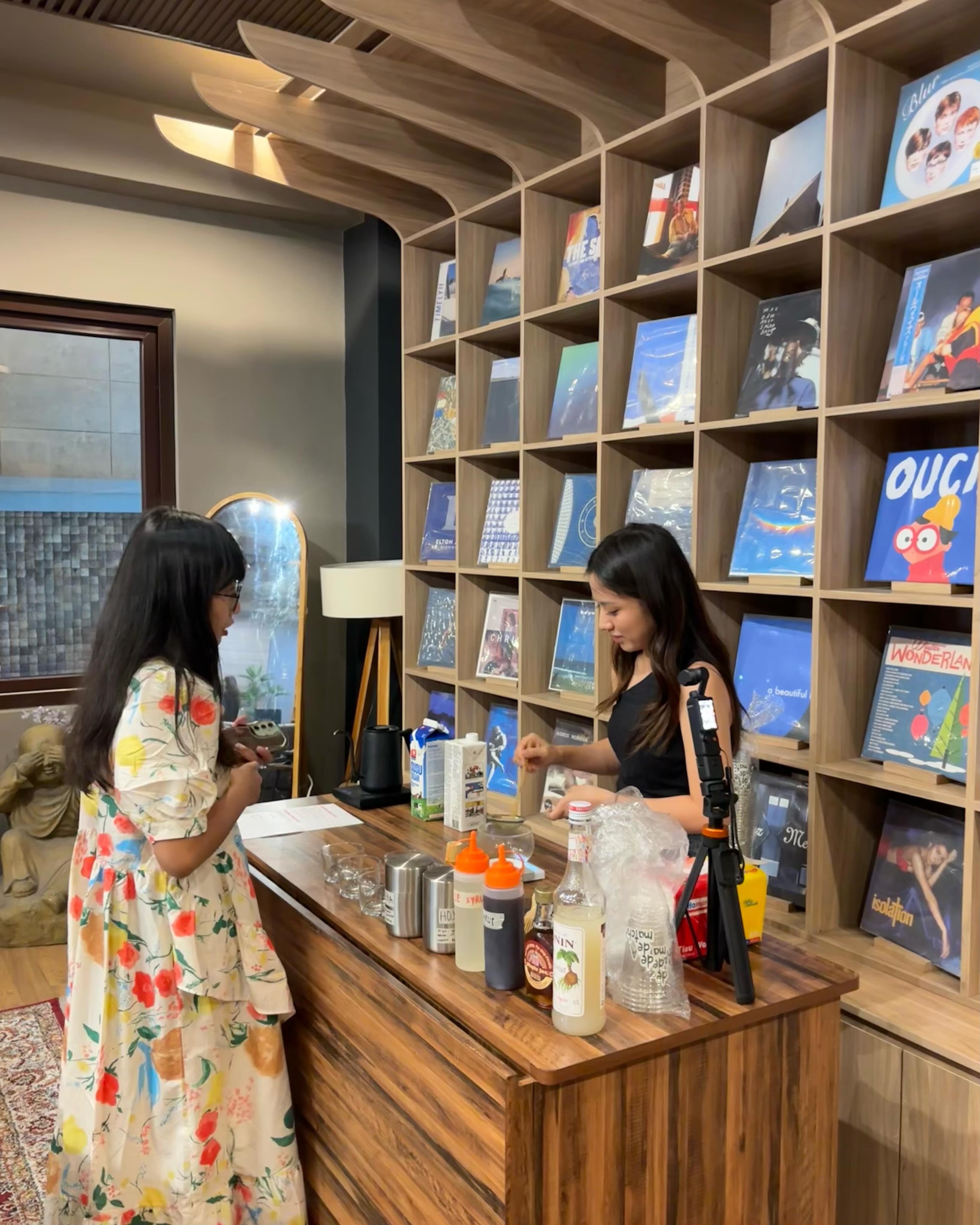 Dua peserta di meja depan Analogue Listening Space, di depan rak tinggi berisi zine dan komik.